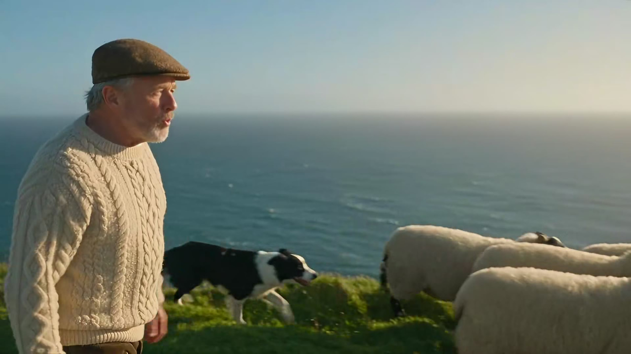 Frame from a Seedance 2.5 Reference sample made in Imagera Sandbox: a grey-bearded shepherd in a cable-knit sweater on sea cliffs with his sheepdog and flock