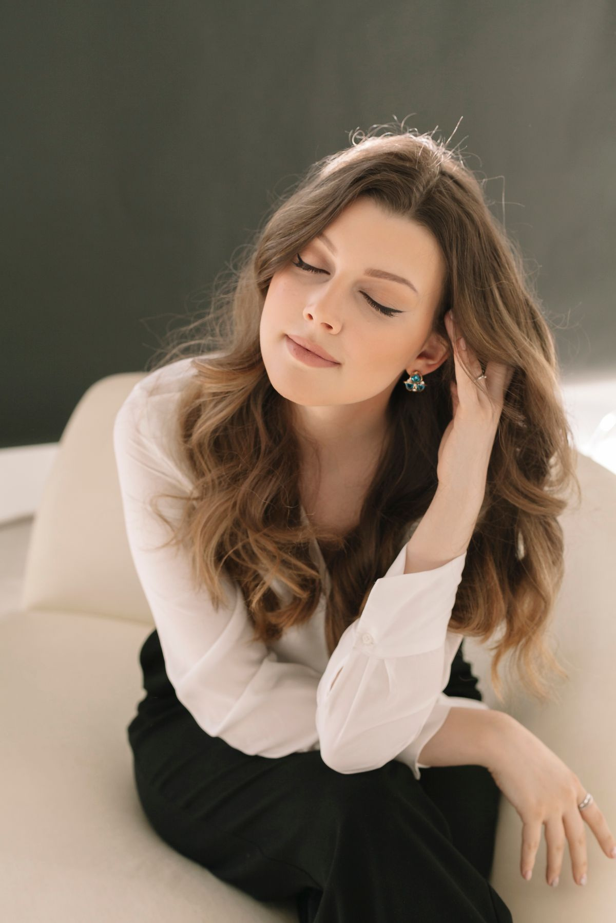 A woman in a white blouse sitting on a cream sofa with both eyes closed and her mouth in a flat line — the frame the shutter caught mid-blink
