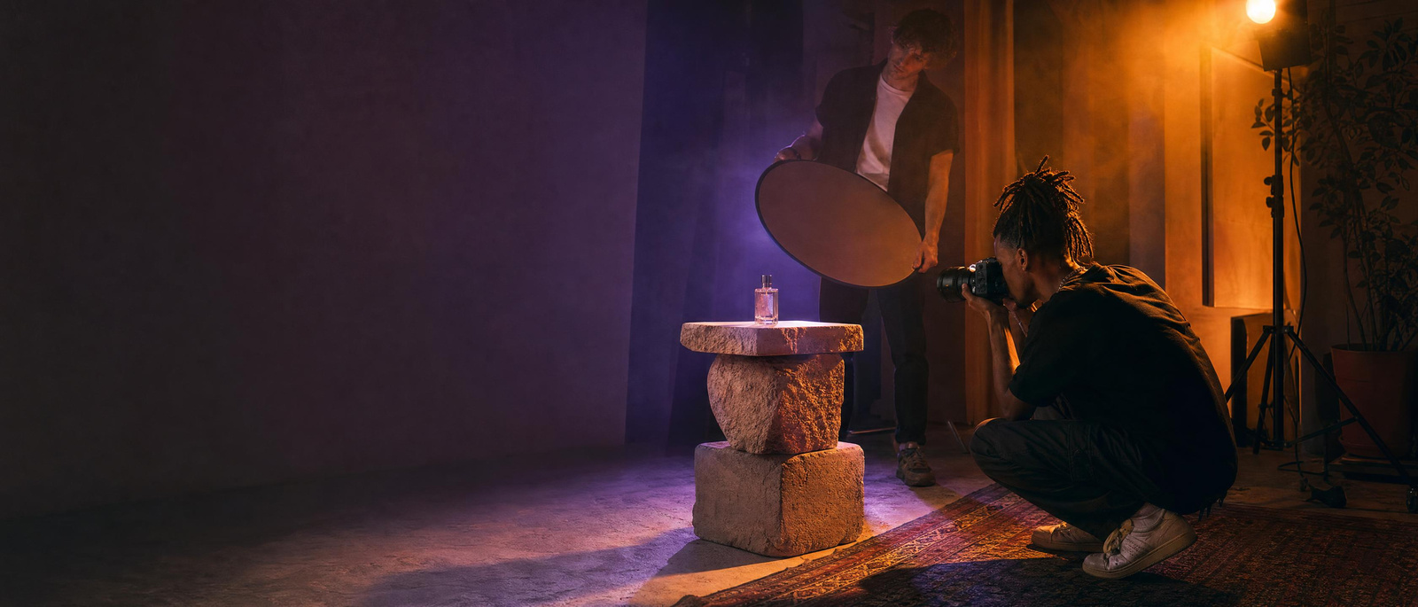 A young photographer shooting a perfume bottle with coloured light