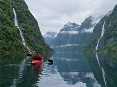 Red kayak on a still fjord between steep green mountains