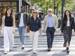 Pedestrians crossing a sunny city street, several faces towards the camera