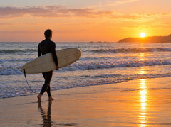 Surfer carrying a board along the shoreline at sunrise