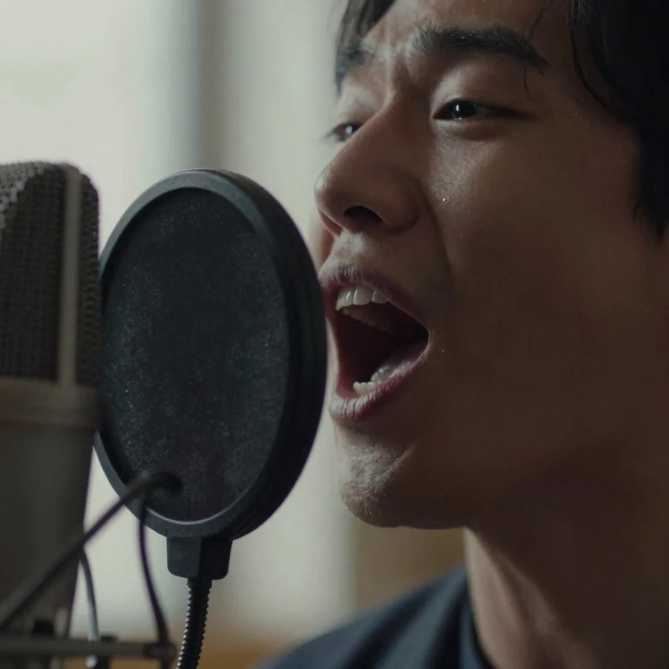 Extreme close-up of a singer's open mouth mid-note beside a pop filter and the grille of a large-diaphragm microphone
