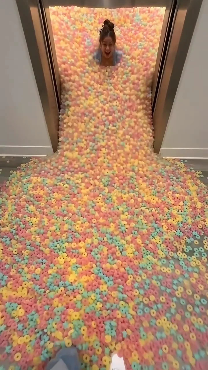 Elevator doors slide open and an avalanche of pastel gummy rings bursts out across a lobby floor, then a young woman wades out and pushes a fuchsia BLIPZ candy pouch into the lens.