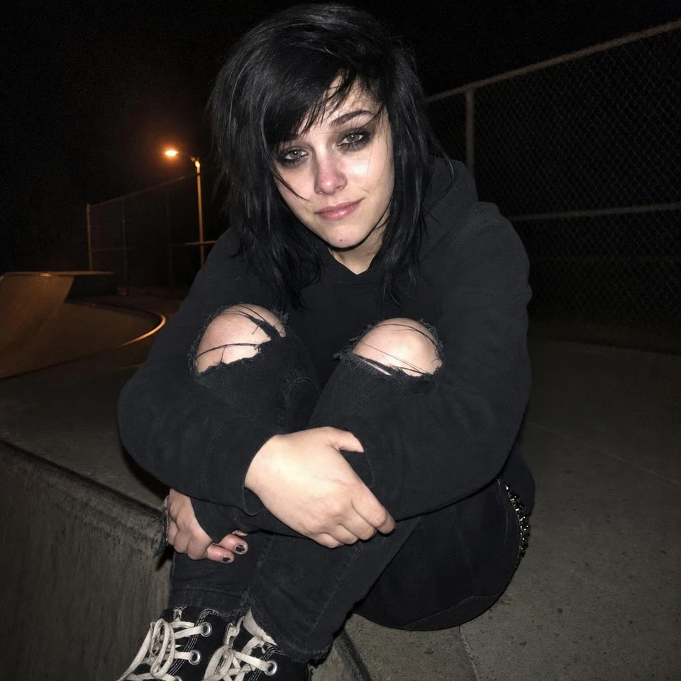 雨夜旧友, a late-night pop playlist in Mandarin Chinese: A young woman with choppy black hair and smudged eyeliner hugs her knees on a skatepark ramp at night, lit by phone flash under an orange streetlight.