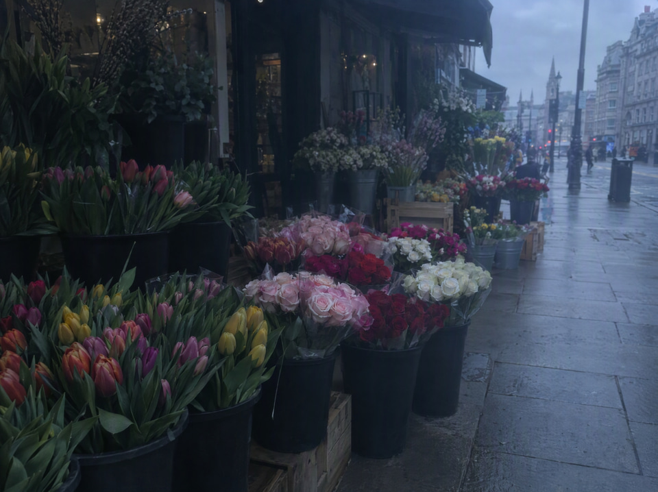 Before: Flat, underexposed phone photo of a flower stall on an overcast street — enhanced