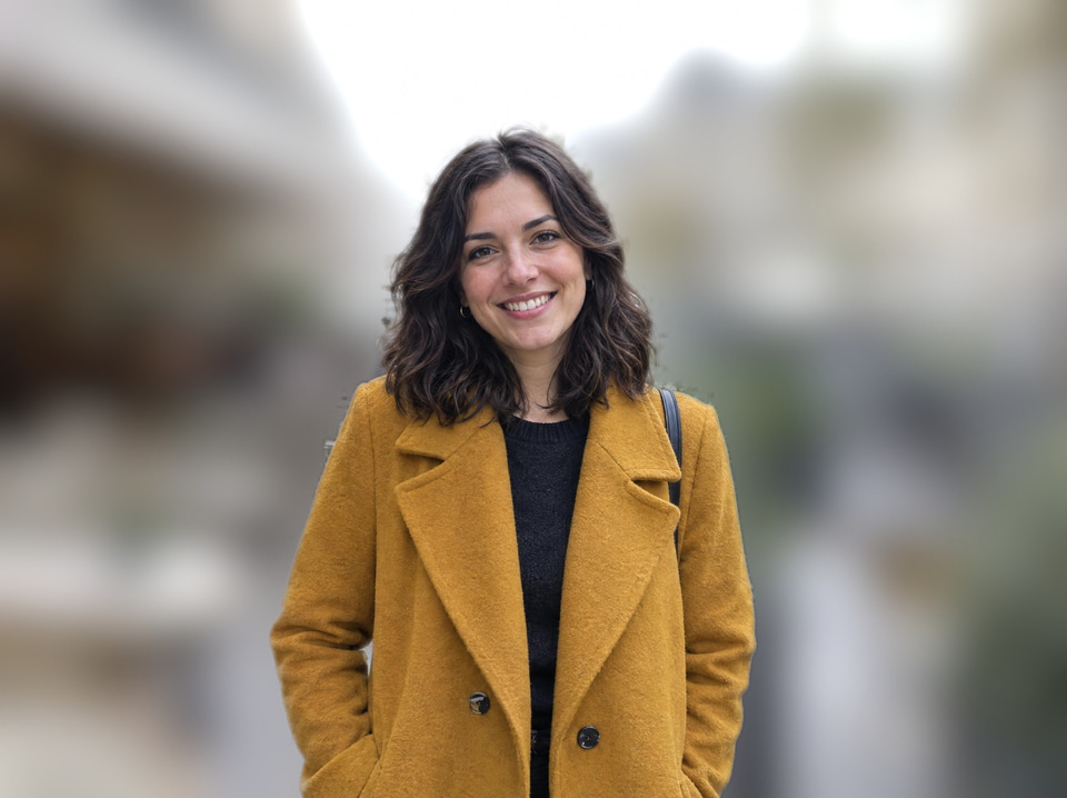 After: Smiling woman in a mustard coat on a busy café terrace — background blurred