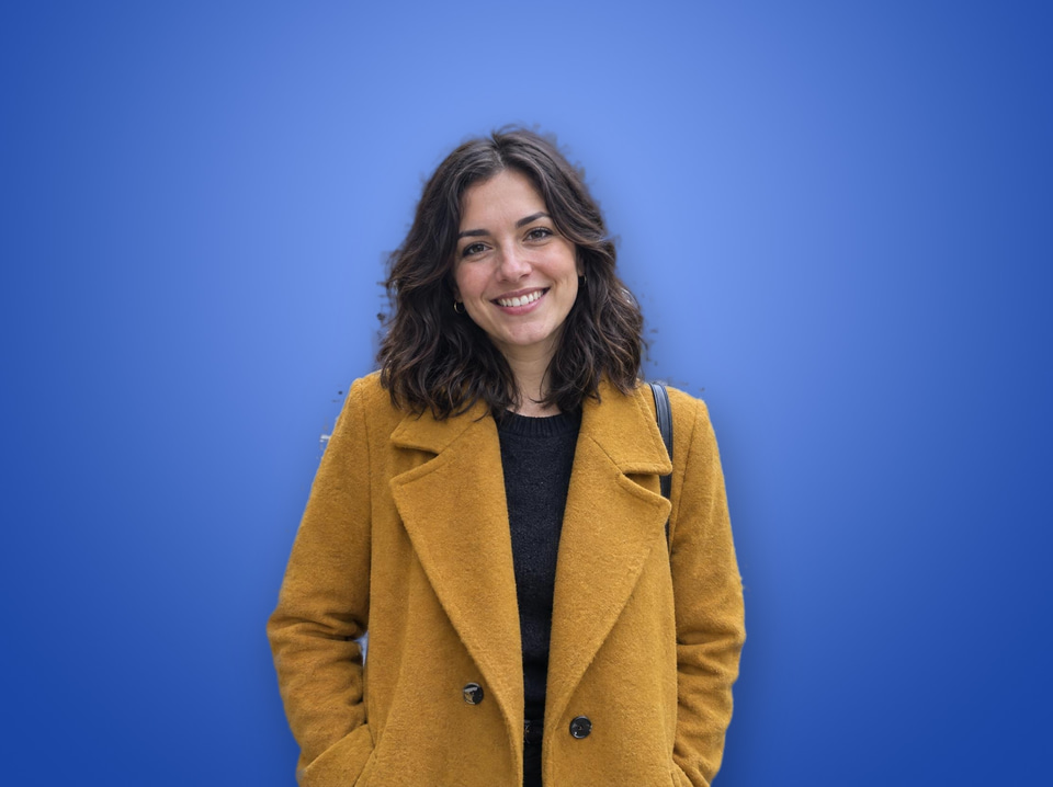 After: Smiling woman in a mustard coat on a busy café terrace — new background colour