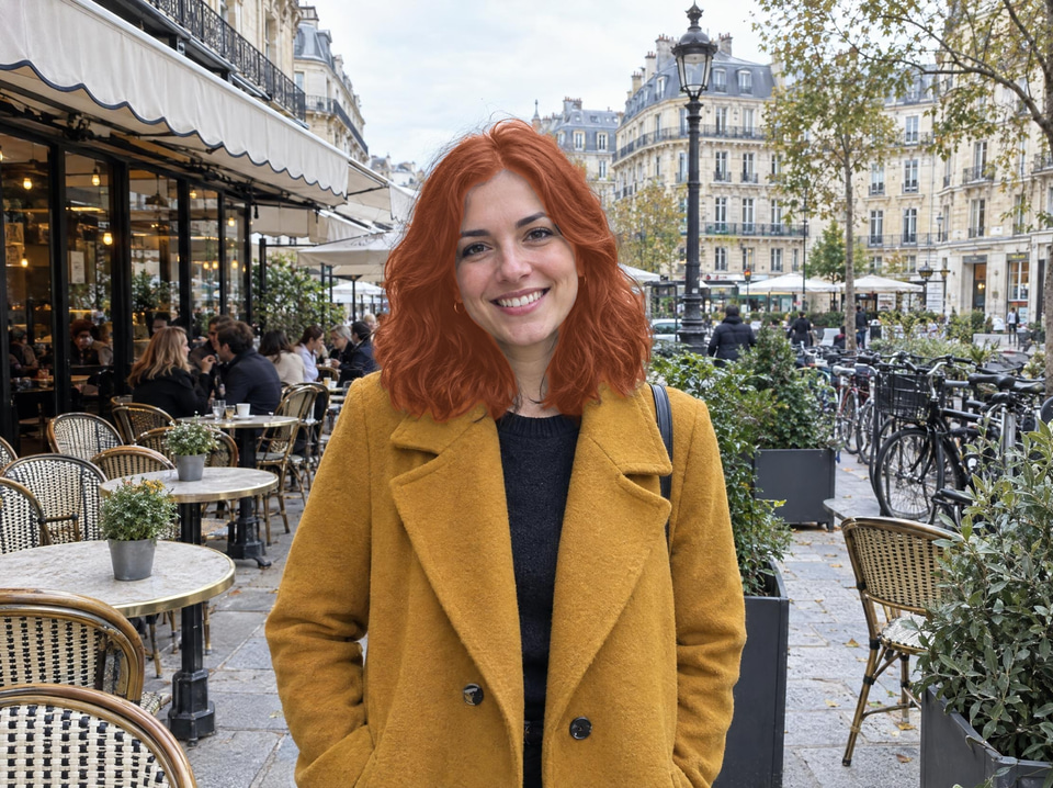 After: Smiling woman in a mustard coat on a busy café terrace — new hair colour