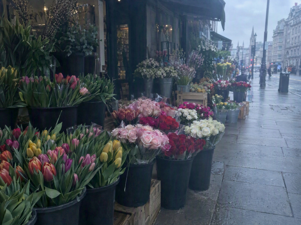 After: Flat, underexposed phone photo of a flower stall on an overcast street — enhanced