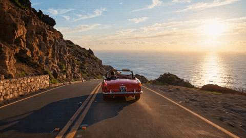 Red convertible driving a cliff-top coast road at sunset — turned into a GIF