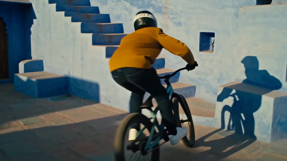 A trials rider hops his bike up indigo steps in Jodhpur's blue city at low sun. — made with Imagera Hermes Max