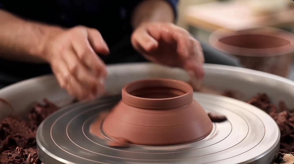 A potter's wet hands lift a spinning clay bowl in warm workshop light. — made with Kandinsky 6 Lite