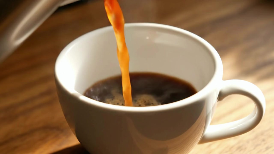 Veo 3.1: Close-up of fresh coffee pouring into a white ceramic cup on a wooden counter, the crema swirling, steam rising in morning light, a slow push-in.