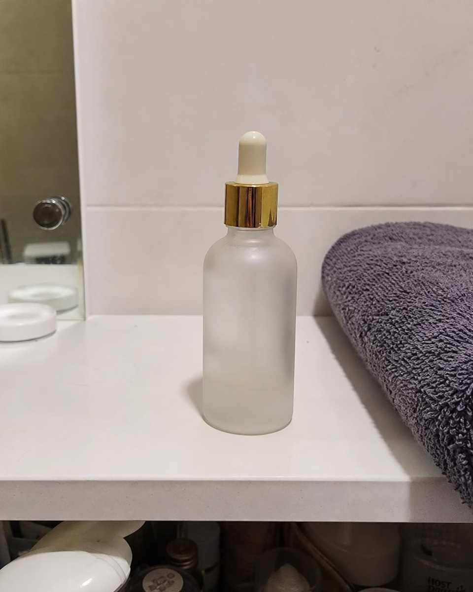 Input: A young creator showing the same serum to her phone camera, made from the product photo