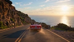 Red convertible driving a cliff-top coast road at sunset