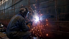 Welder working on a ship hull with bright sparks flying